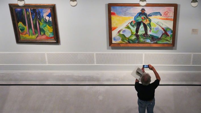 Ein Mann fotografiert mit seinem Smartphone in der Berlinischen Galerie während der Pressevorbesichtigung zur Ausstellung "Edvard Munch. Zauber des Nordens“ das Bild „Der Mann im Kohlacker“ (1943, l auf Leinwand). Links hängt „Der Wald“ (1927, l auf Leinwand).