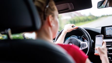 Eine junge Frau hält während der Fahrt ihr Smartphone in der Hand