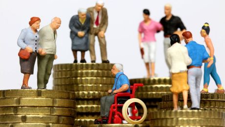 Miniatur-Figuren aller Altersgruppen stehen auf Münzstapeln © imago images/Ralph Peters