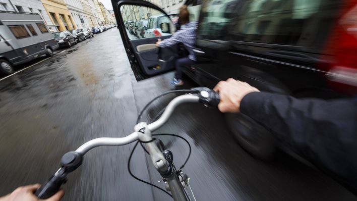 Ein Radfahrer weicht einer offenen Autotür auf der Straße aus © imago images/photothek/Thomas Trutschel