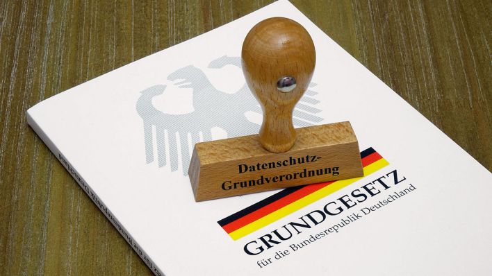 Ein Stempel mit Aufschrift "Datenschutz-Grundverordnung" liegt auf einer Ausgabe des Grundgesetz © imago images/Steinach