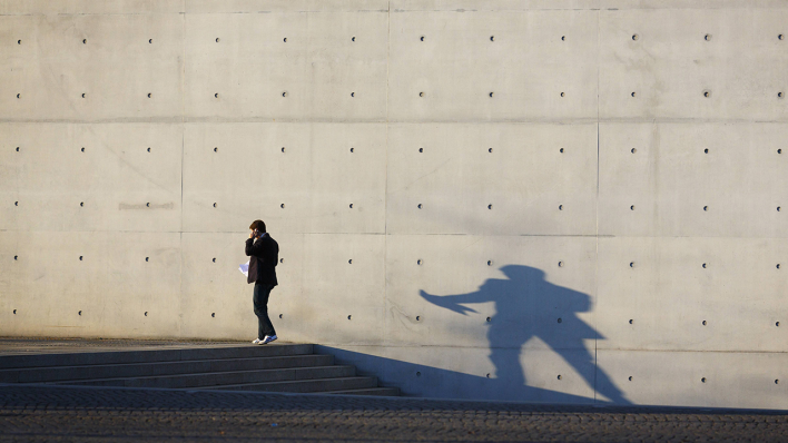 Eine Person telefoniert vor einer Betonwand und wirft dabei einen Schatten © imago/photothek