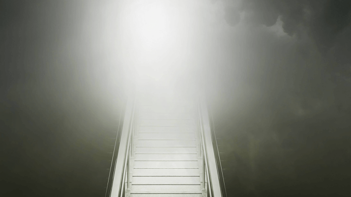 Stufen auf einer Rolltreppe führen zu glühendem Licht in bewölktem Himmel © imago images/Ikon Images