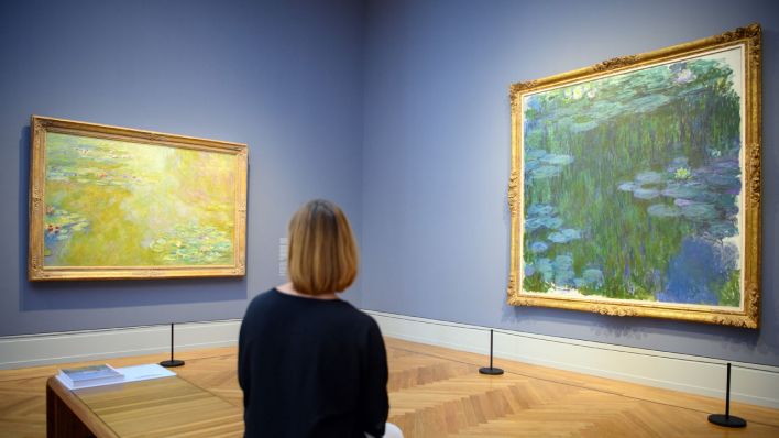 Eine Frau betrachtet während des Rundgangs zur Eröffnung der neuen Ausstellung "Impressionismus. Die Sammlung Hasso Plattner" im Museum Barberini die Gemälde "Der Seerosenteich" (l, etwa 1918) und "Seerosen" (1914 - 1917) von Claude Monet © dpa/Soeren Stache