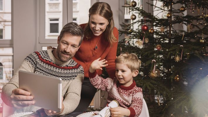 Eine Familie sitzt mit einem Tablet vor dem Weihnachtsbaum