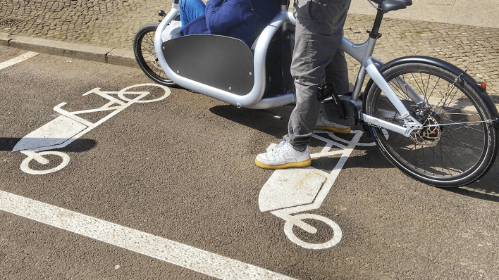 Ein Mann steht mit seinem Lastenrad auf einem Parkplatz für Lastenräder © radioeins/Chris Melzer