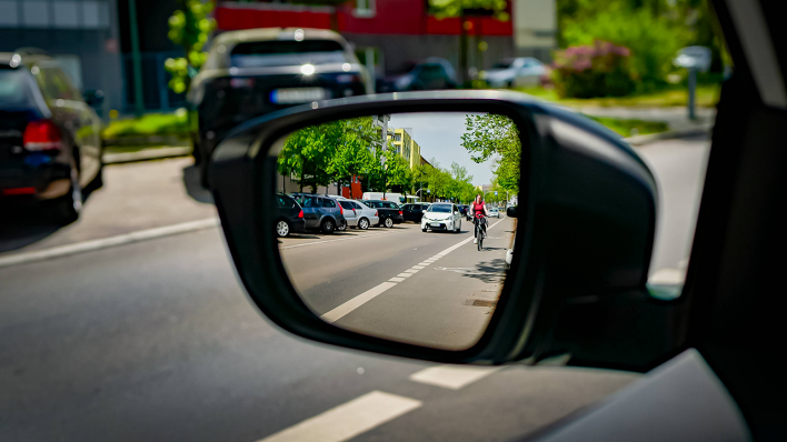 Eine Radfahrerin ist im Rückspiegel eines Autos zu sehen