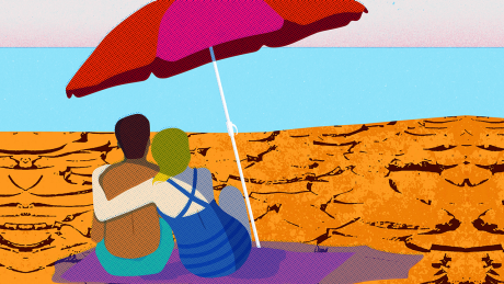 Ein Paar sitzen einem unter Sonnenschirm an einem trockenen, rissigen Strand © imago images/Ikon Images