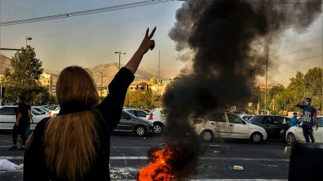 Eine Frau steht in Teheran während einer Demonstration nach dem Tod der 22-jährigen Mahsa Amini vor einem brennenden Autoreifen und zeigt das Victory-Zeichen © Uncredited/AP/dpa