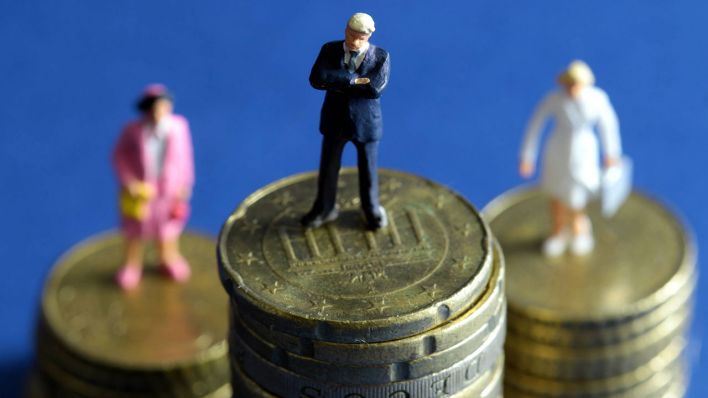 Miniatur-Figuren stehen auf unterschiedlich hohen Münzstapeln