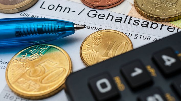 Auf einer Lohnabrechnung liegen Münzen, ein Kugelschreiber und ein Taschenrechner (Symbolbild) © imago images/Zoonar