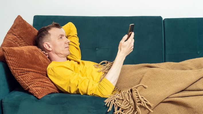Ein Mann liegt auf einem Sofa und schaut auf ein Smartphone © IMAGO / Panthermedia / Jane Rubtsova