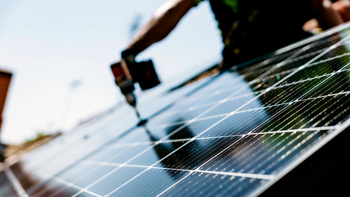 Ein Handwerker befestigt ein Solarpanel auf einem Hausdach © IMAGO / Westend61