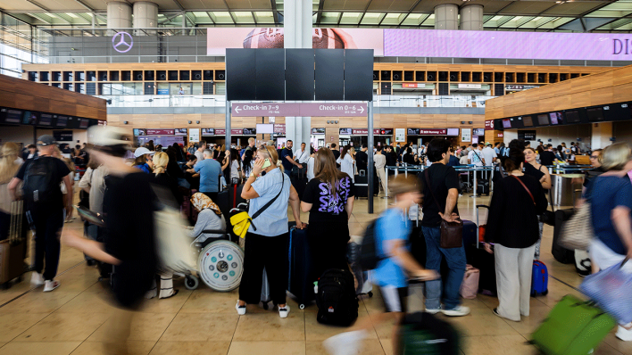 Zahlreiche Fluggäste warten am Hauptstadtflughafen BER vor einer schwarzen Anzeigetafel. Am Flughafen BER ist der Flugverkehr eingestellt worden © picture alliance/dpa|Christoph Soeder