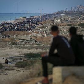Zwei Jungen beobachten eine Gruppe von Palästinensern, die inmitten von zerstörten Gebäuden in den nördlichen Gazastreifen zurückkehren © Abdel Kareem Hana/AP/dpa