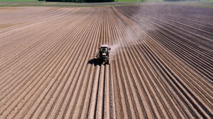Ein Traktor zieht bei der Bearbeitung eines Kartoffelfeldes eine Staubfahne hinter sich her © imago images/Jochen Eckel