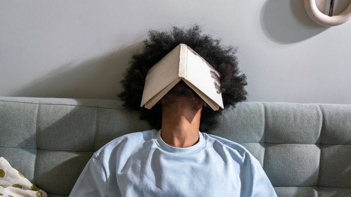 Ein Mann schläft mit einem Buch auf dem Kopf © IMAGO/Westend61