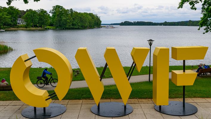 Buchstaben «OWF», als Abkürzung für das Ostdeutsche Wirtschaftsforum, stehen am Ufer des Scharmützelsees. © picture alliance/dpa | Patrick Pleul