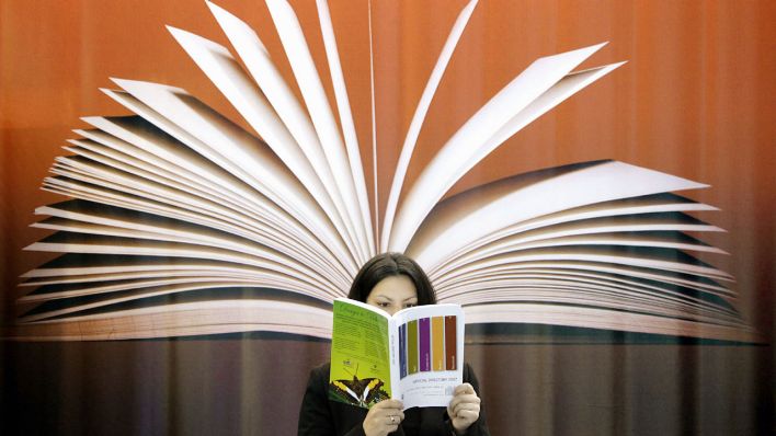 Schöner Lesen: Eine Frau liest vor einem Plakat mit einem aufgefächerten Buch